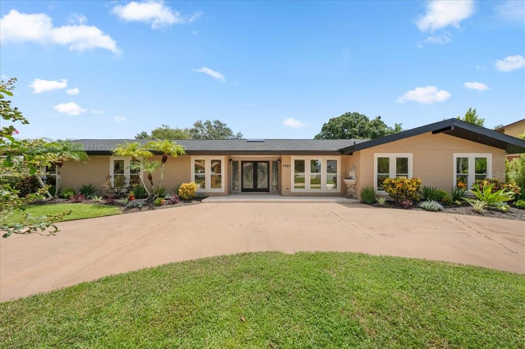 A single-story house with a tan stucco exterior, dark roof, and a curved concrete driveway — 1701 ALLENS CREEK DRIVE, CLEARWATER, FL