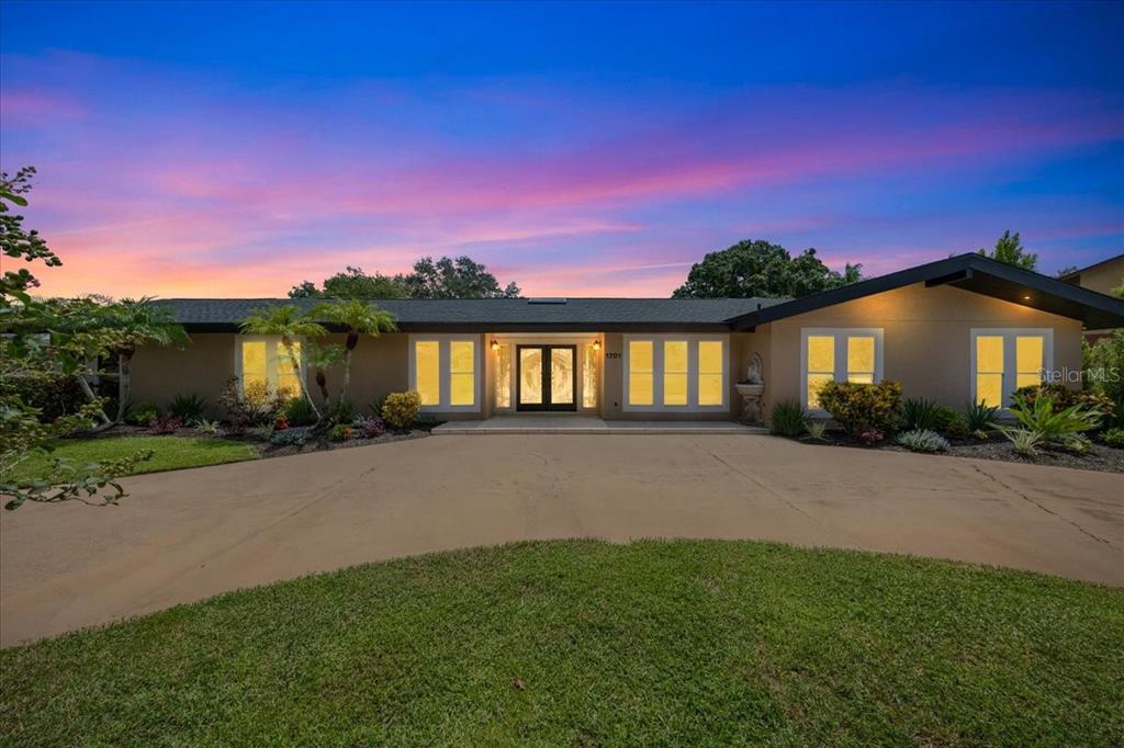 A single-story house with a flat roof and a large concrete driveway at sunset — 1701 ALLENS CREEK DRIVE, CLEARWATER, FL