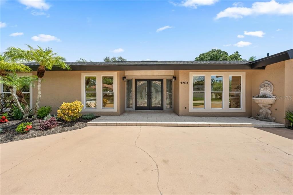 A single-story house with a tan stucco exterior, double front doors, and a paved driveway — 1701 ALLENS CREEK DRIVE, CLEARWATER, FL