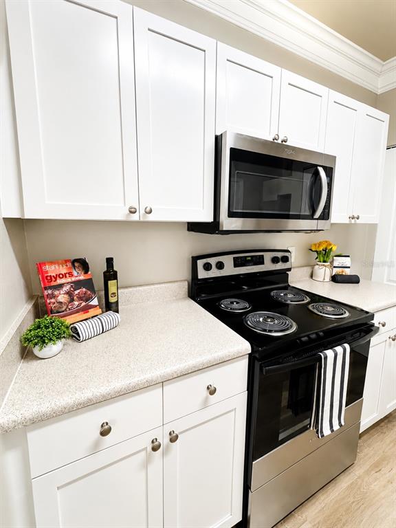 A kitchen features white cabinets, a stainless steel microwave, and a black electric range — 8813 VILLA VIEW CIRCLE UNIT 204, ORLANDO, FL