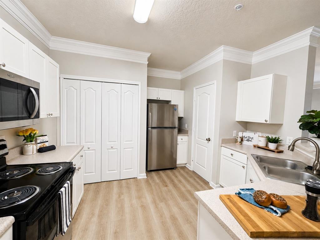 A kitchen with white cabinets, stainless steel appliances, light countertops, and wood-look flooring — 8813 VILLA VIEW CIRCLE UNIT 204, ORLANDO, FL