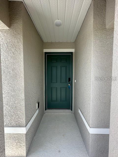 A covered entryway features a dark green front door set between textured beige walls — 2432 NW 22ND COURT, OCALA, FL