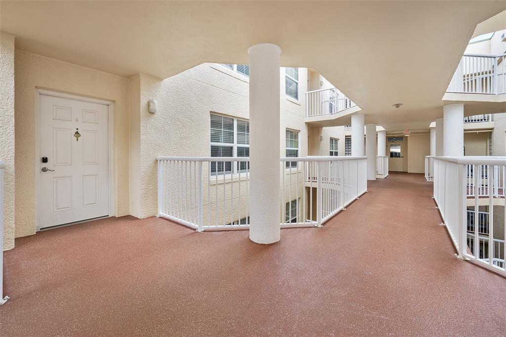 An outdoor apartment building walkway with white railings, a white door, and textured flooring — 4670 LINKS VILLAGE DRIVE UNIT B606, PONCE INLET, FL