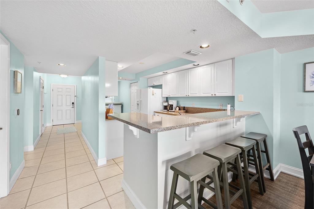 A kitchen with white cabinets, granite countertops, and a breakfast bar with three stools — 4670 LINKS VILLAGE DRIVE UNIT B606, PONCE INLET, FL