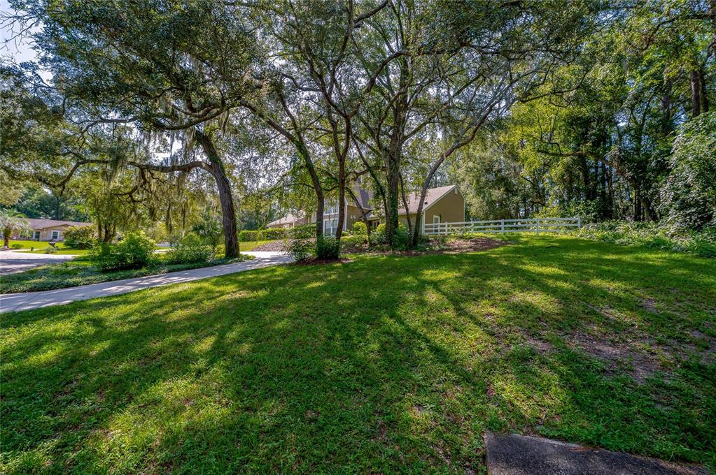 A grassy front yard with large oak trees leads to a house with a white fence — 2081 PENNSYLVANIA DRIVE, DELAND, FL
