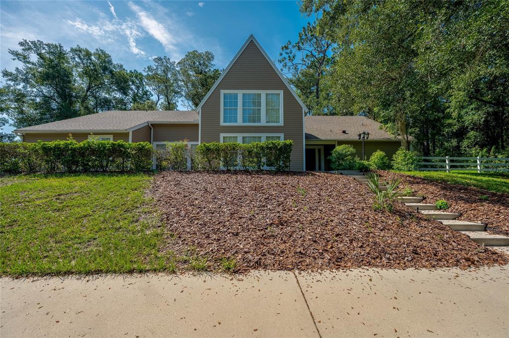 A two-story house with tan siding and a brown shingled roof sits behind a landscaped yard — 2081 PENNSYLVANIA DRIVE, DELAND, FL
