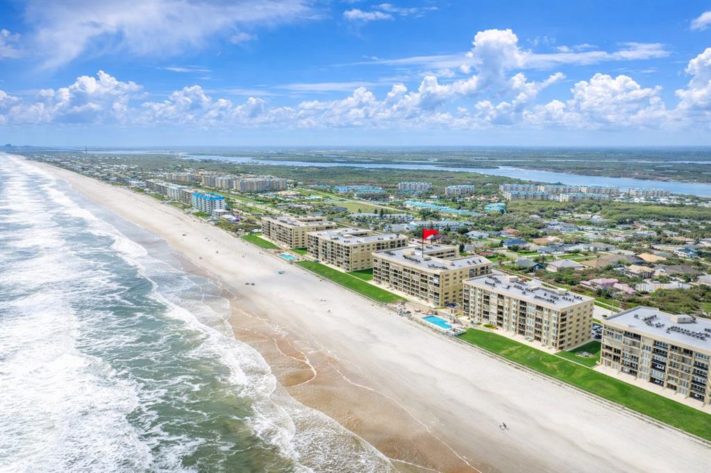 An aerial view shows five beachfront apartment buildings with swimming pools along a sandy shore — 4555 S ATLANTIC AVENUE UNIT 4506, PONCE INLET, FL