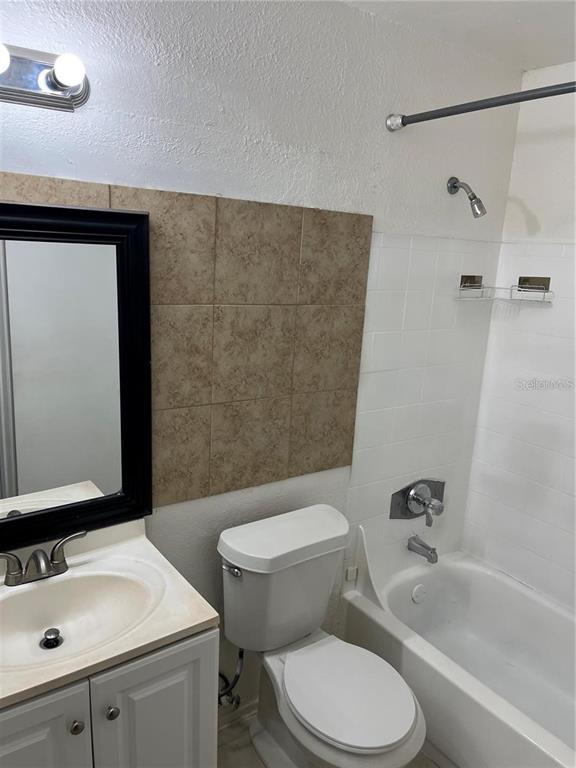 A bathroom features a vanity with a mirror, a toilet, and a white tiled shower — 1924 LAKE ATRIUMS CIRCLE UNIT 55, ORLANDO, FL