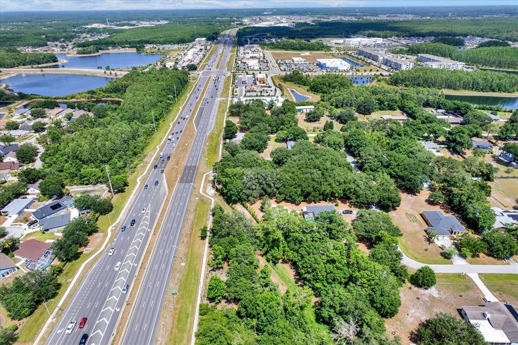 An aerial view shows a multi-lane highway running through a suburban area with wooded lots — STATE ROAD 54, LUTZ, FL