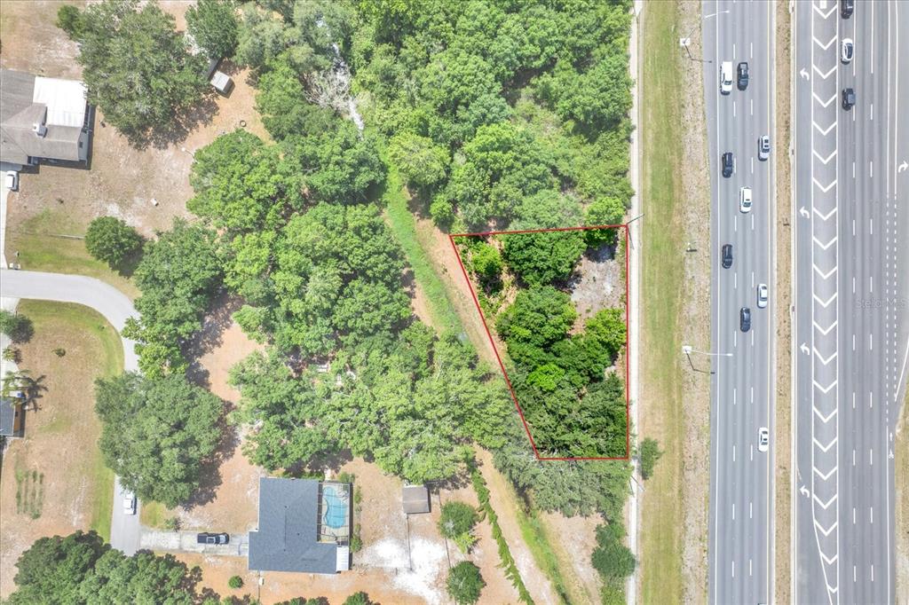 An aerial view shows a triangular, wooded plot of land adjacent to a multi-lane highway — STATE ROAD 54, LUTZ, FL