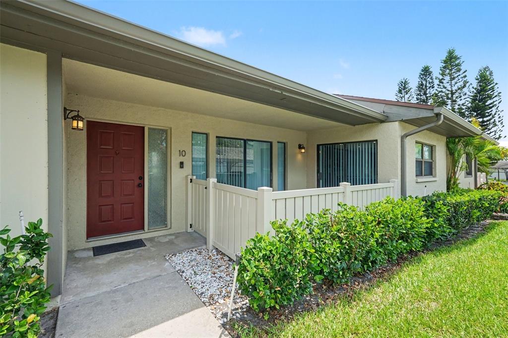A single-story residential building with a tan stucco exterior, a red front door, and landscaping — 10 LESLEY LANE, OLDSMAR, FL