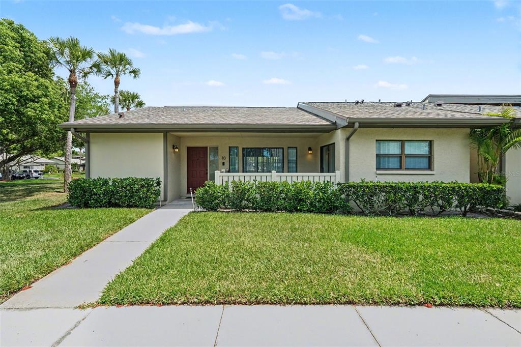 A red front door with a white fence and landscaping sits under a covered porch — 10 LESLEY LANE, OLDSMAR, FL