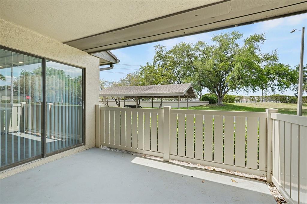 A covered patio with a light-colored fence overlooks a grassy area and a carport — 10 LESLEY LANE, OLDSMAR, FL