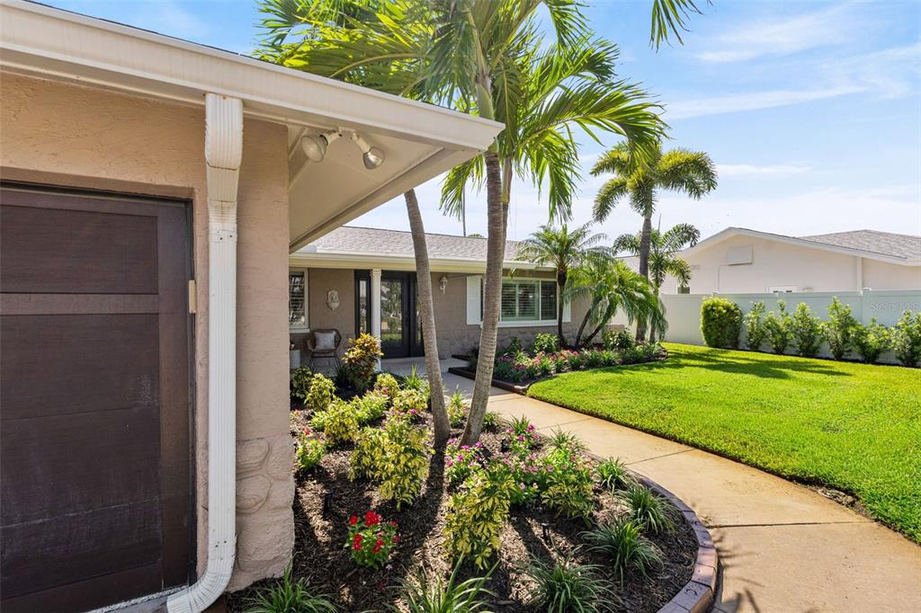 A view of a house exterior featuring a garage, landscaped garden, and a palm tree — 251 N JULIA CIRCLE, ST PETE BEACH, FL