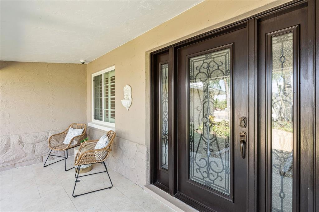A covered porch features two wicker chairs, a window, and a dark wood front door — 251 N JULIA CIRCLE, ST PETE BEACH, FL