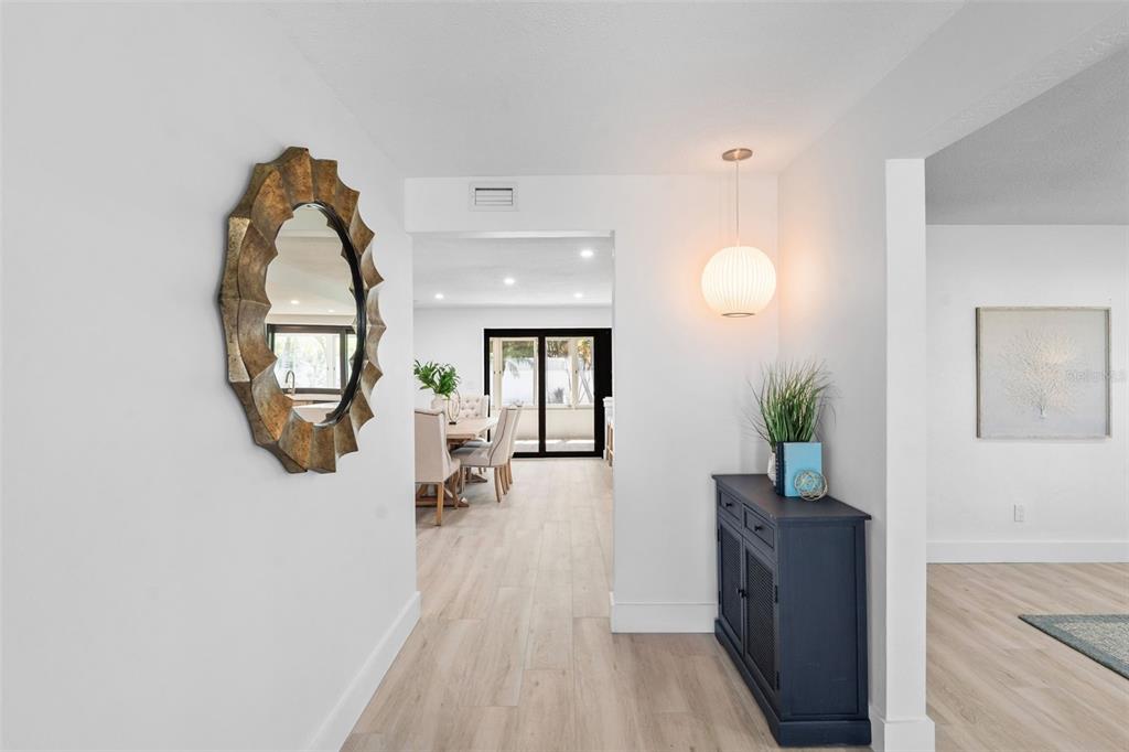 A bright entryway features light wood-look flooring, a dark blue cabinet, and a sunburst mirror — 251 N JULIA CIRCLE, ST PETE BEACH, FL