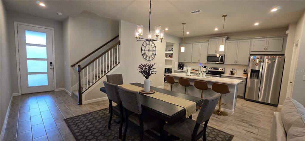 An open-concept kitchen and dining area features gray cabinetry, stainless steel appliances, and a staircase — 4100 CLOUD HOPPER WAY, LUTZ, FL
