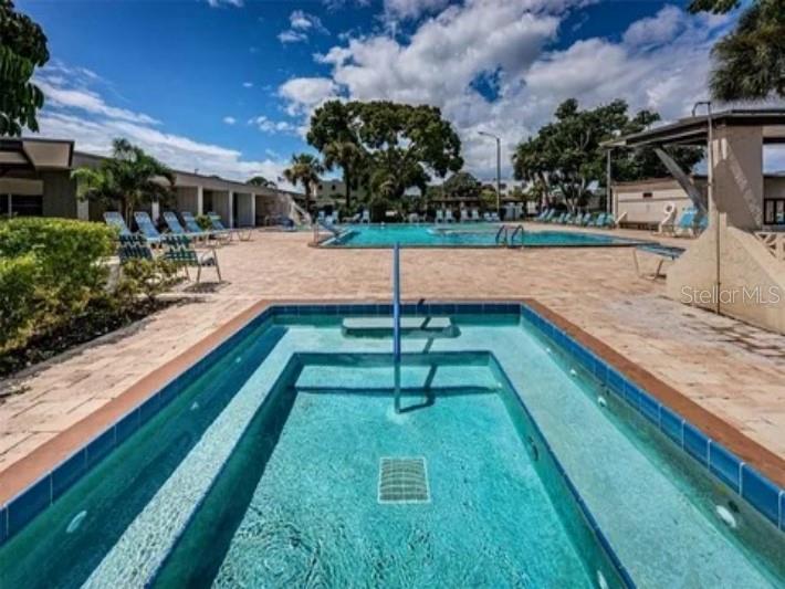 A rectangular hot tub sits in the foreground with a larger swimming pool behind it — 5925 TERRACE PARK DRIVE N UNIT 111, ST PETERSBURG, FL