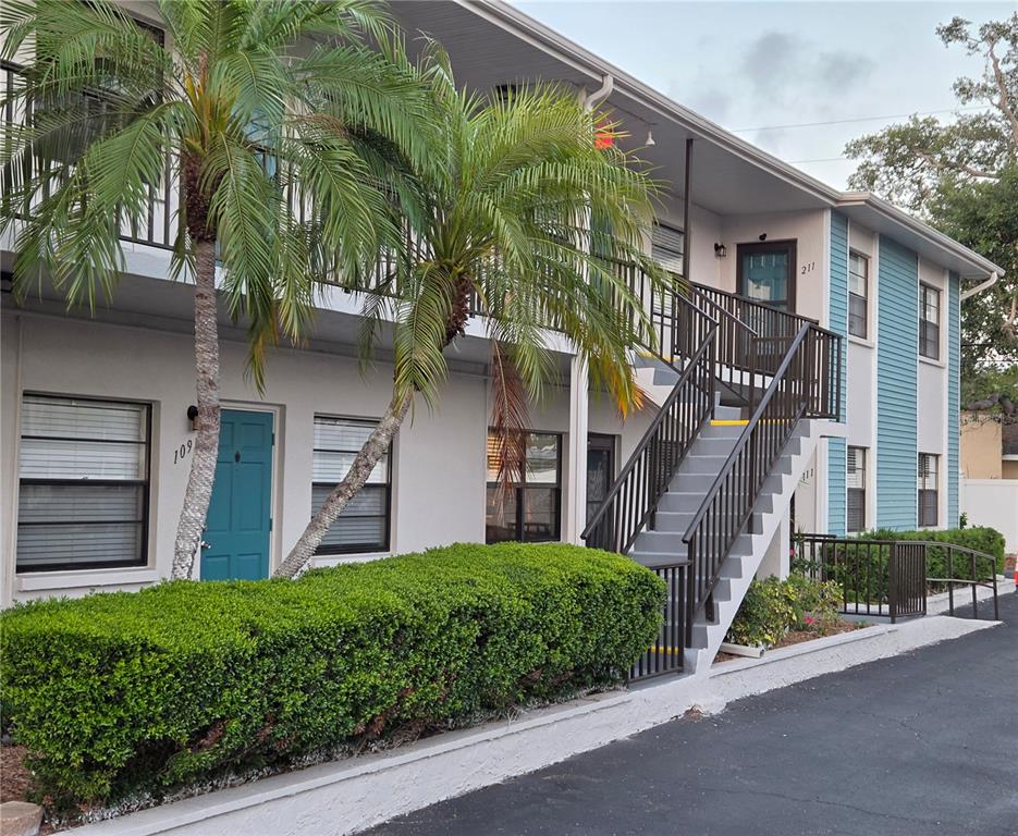 The exterior of a two-story apartment building features a teal door, stairs, and palm trees — 5925 TERRACE PARK DRIVE N UNIT 111, ST PETERSBURG, FL