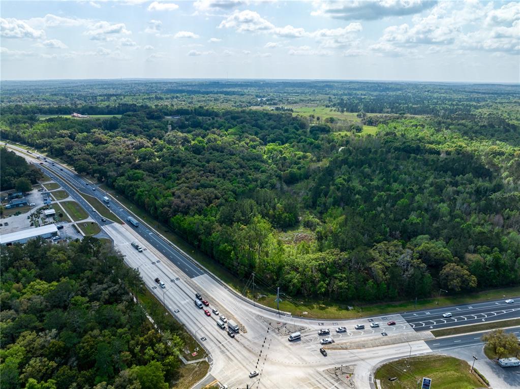 An aerial view shows a multi-lane highway intersection adjacent to a large, wooded plot of land — 22374 CORTEZ BOULEVARD, BROOKSVILLE, FL