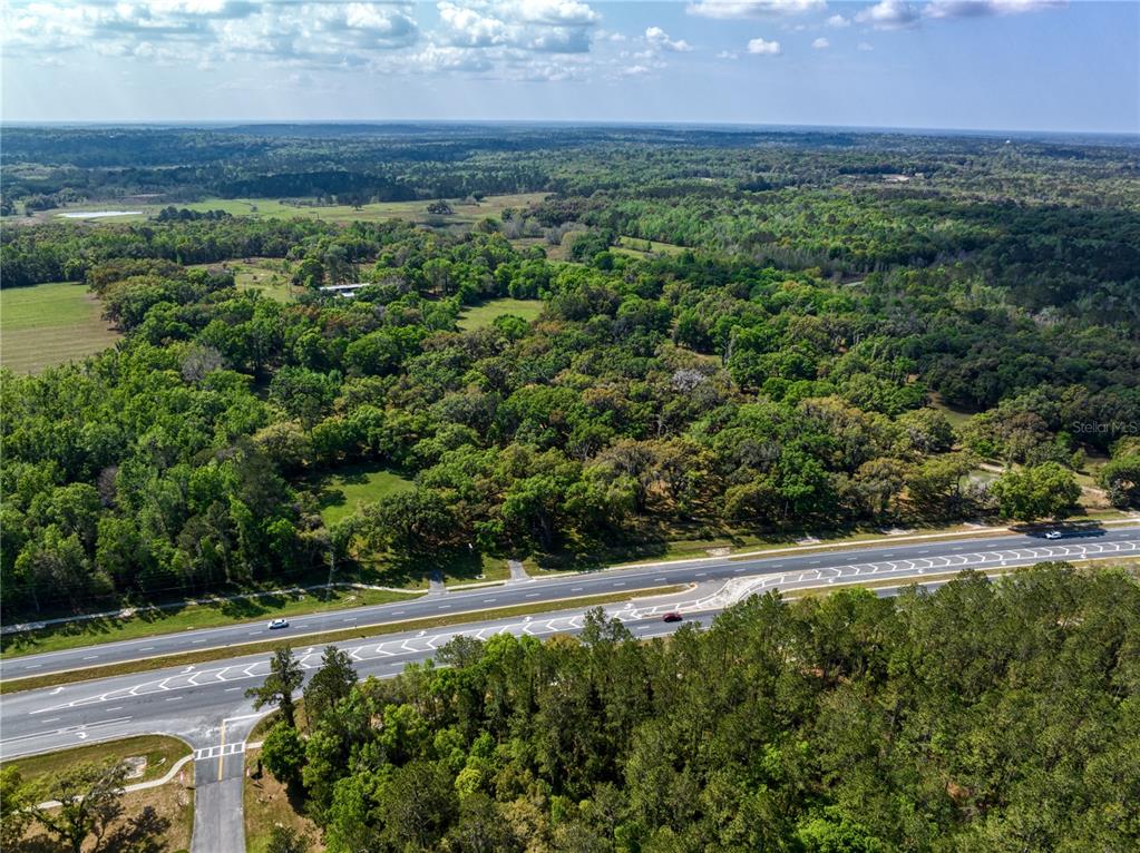An aerial view shows a multi-lane highway bordering a large, wooded plot of land — 22374 CORTEZ BOULEVARD, BROOKSVILLE, FL