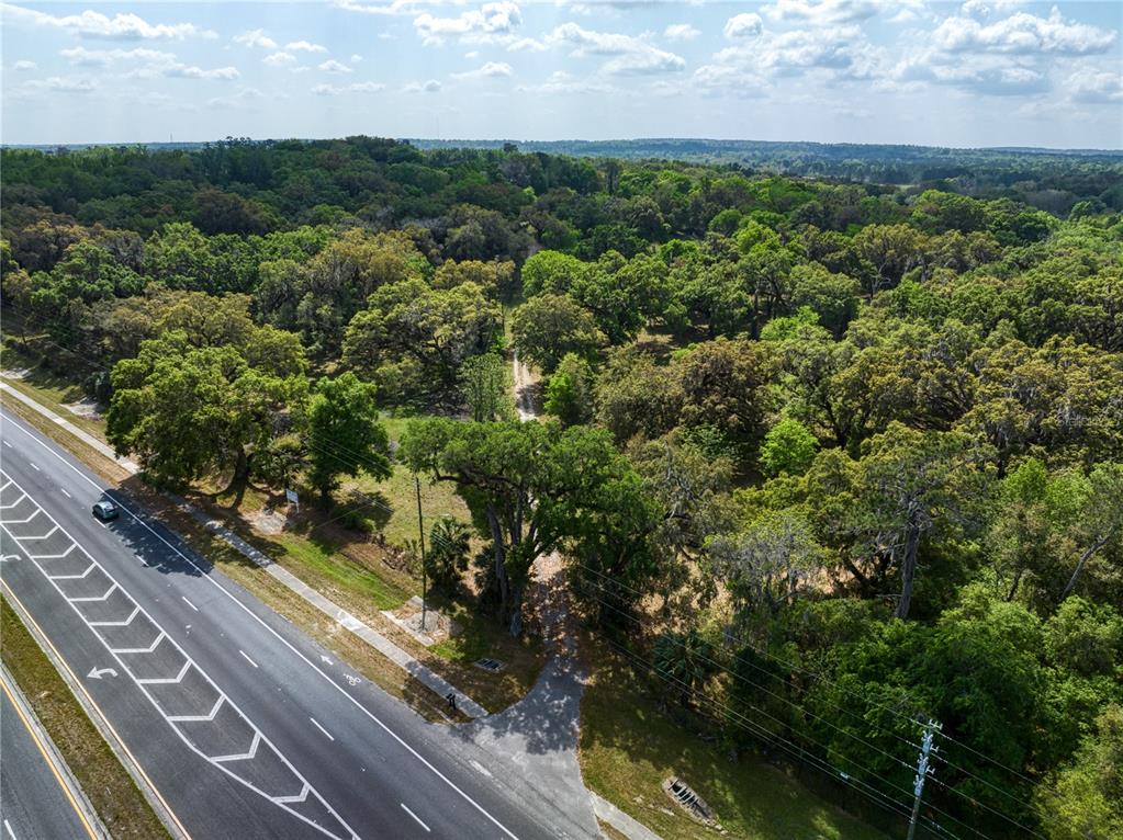 An aerial view shows a wooded lot adjacent to a multi-lane paved road — 22374 CORTEZ BOULEVARD, BROOKSVILLE, FL