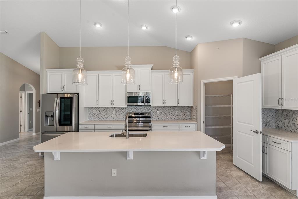 A modern kitchen features white cabinets, stainless steel appliances, a quartz island, and tile flooring — 4 TIDEWAY TRAIL, PALM COAST, FL