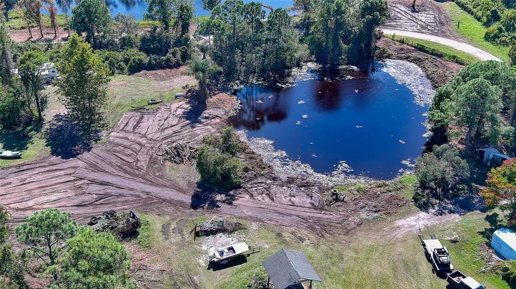 An aerial view shows a pond surrounded by cleared land, trees, and parked vehicles — 806 W ARIEL ROAD, EDGEWATER, FL