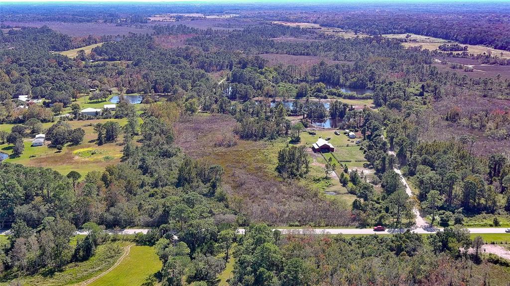 An aerial view shows a rural property with a red barn, ponds, and surrounding woods — 806 W ARIEL ROAD, EDGEWATER, FL