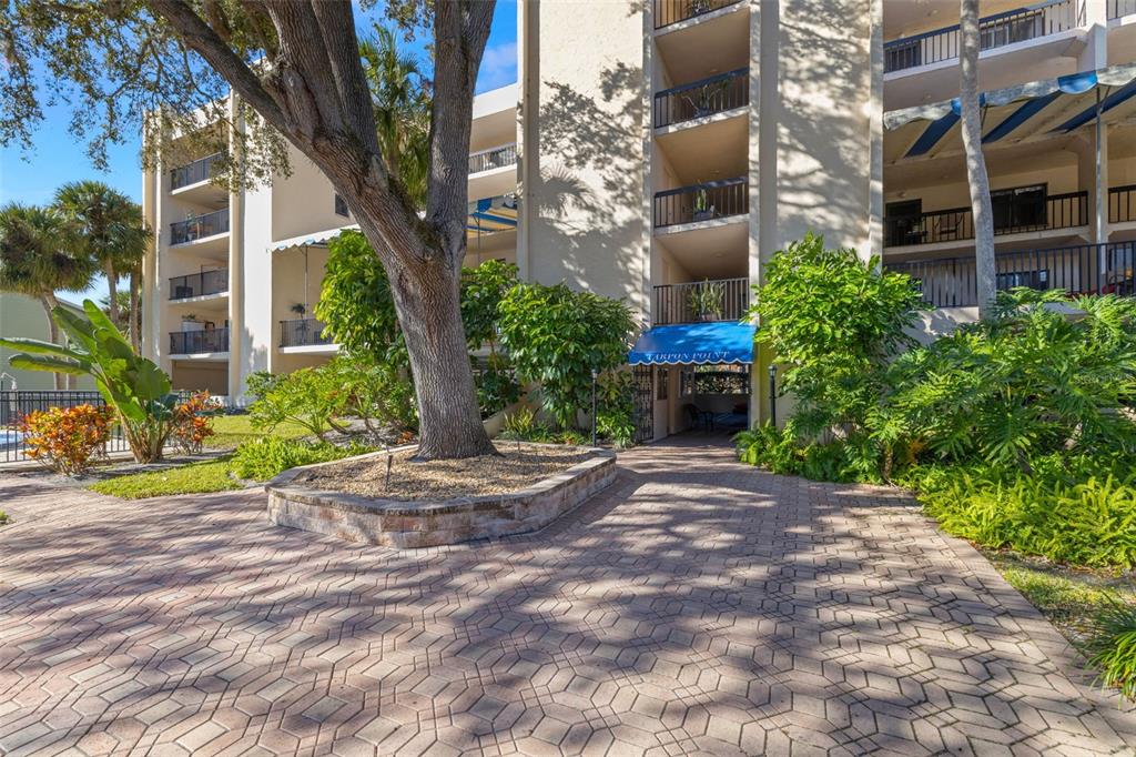 A paved walkway leads to the entrance of a multi-story apartment building with balconies — 402 TARPON POINT, TARPON SPRINGS, FL