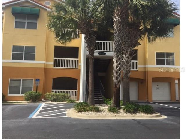 A three-story apartment building with yellow stucco walls, balconies, and palm trees in front — 10764 70TH AVENUE UNIT 1102, SEMINOLE, FL