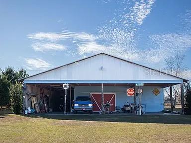 A large, open-sided metal pole barn structure sits on a grassy lot under a blue sky — 1677 W HIGHWAY 316, CITRA, FL