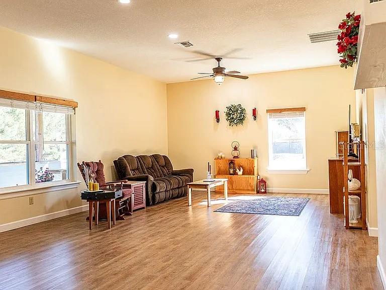 A living room with light-colored walls, wood-look flooring, a brown sofa, and a ceiling fan — 1677 W HIGHWAY 316, CITRA, FL