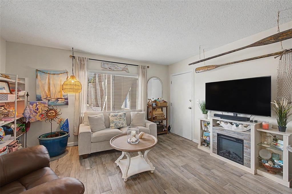 A living room features a sofa, coffee table, television, and fireplace with coastal-themed decor — 2110 GULF BOULEVARD UNIT 6, INDIAN ROCKS BEACH, FL
