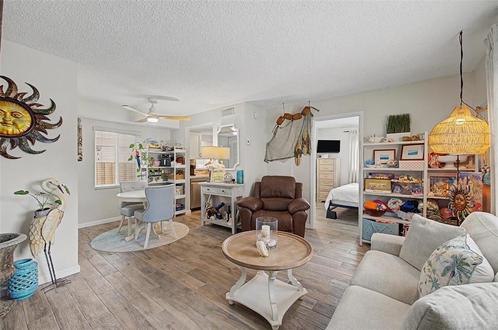 A living room with wood-look tile flooring, a dining area, and an open bedroom doorway — 2110 GULF BOULEVARD UNIT 6, INDIAN ROCKS BEACH, FL