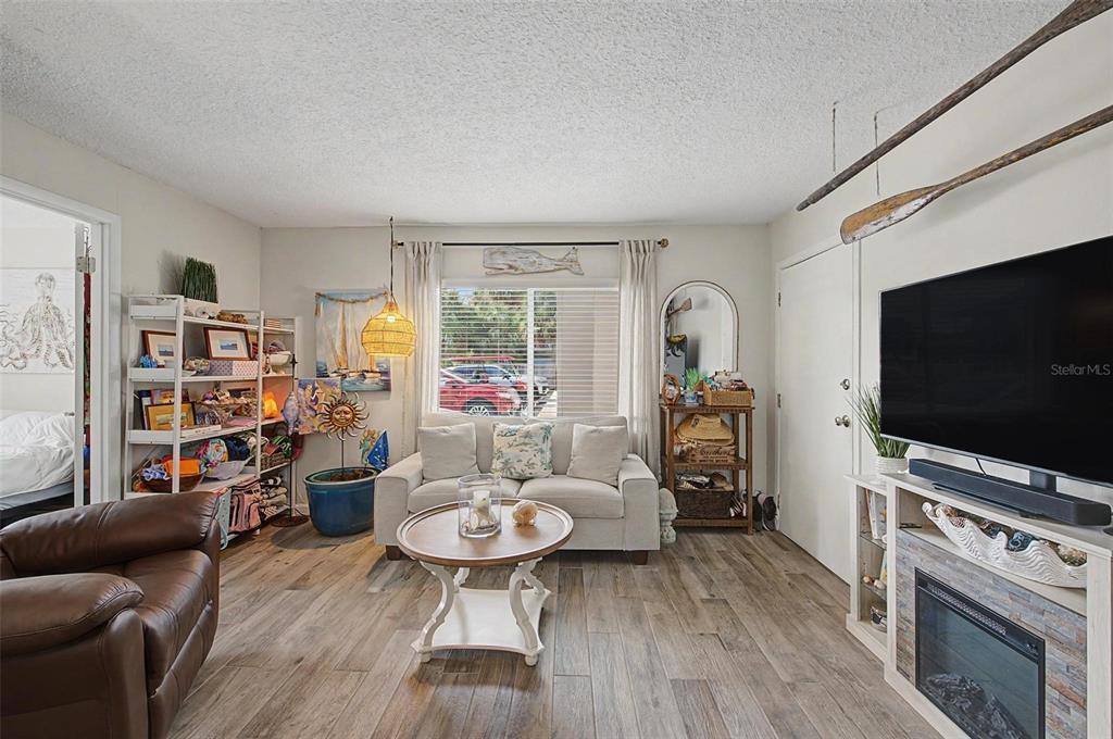 A living room features wood-look flooring, a beige sofa, a fireplace, and coastal-themed decor — 2110 GULF BOULEVARD UNIT 6, INDIAN ROCKS BEACH, FL