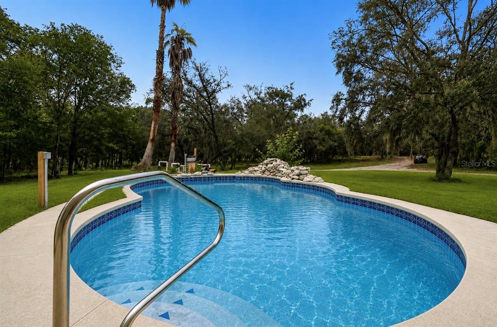 A kidney-shaped swimming pool with a rock water feature sits in a grassy backyard — 17503 GALVESTON STREET, SPRING HILL, FL