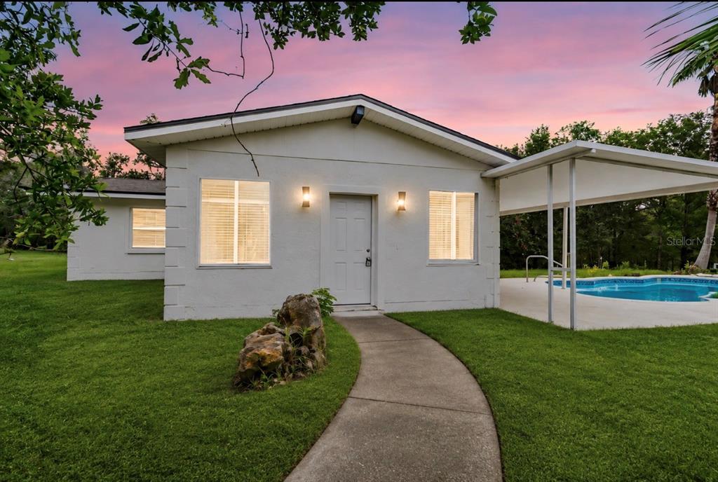 A white single-story house with a concrete walkway, a small pool, and a covered patio — 17503 GALVESTON STREET, SPRING HILL, FL