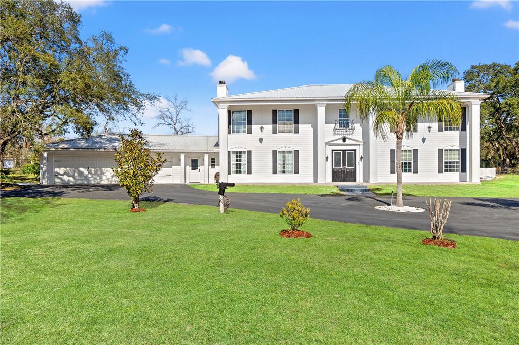 A two-story white house with black shutters and a metal roof sits on a lawn — 14485 SWITCH BACK ROAD, SPRING HILL, FL