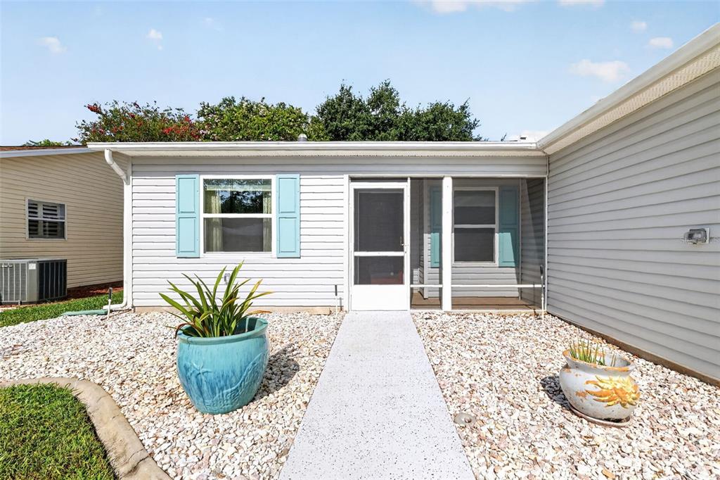 The exterior of a light gray house features a screened porch, blue shutters, and gravel landscaping — 815 GRAND VISTA TRAIL, LEESBURG, FL