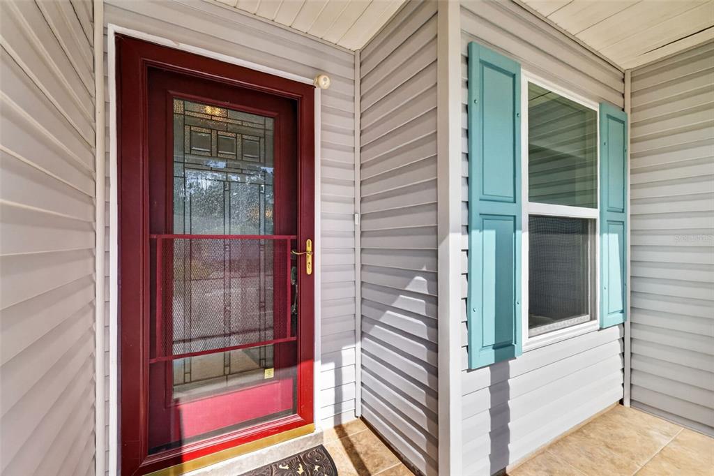 A red front door with a glass insert and storm door next to a shuttered window — 815 GRAND VISTA TRAIL, LEESBURG, FL