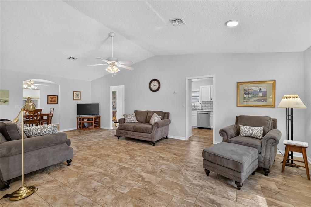 A living room features tile flooring, gray upholstered furniture, and a vaulted ceiling with a fan — 815 GRAND VISTA TRAIL, LEESBURG, FL