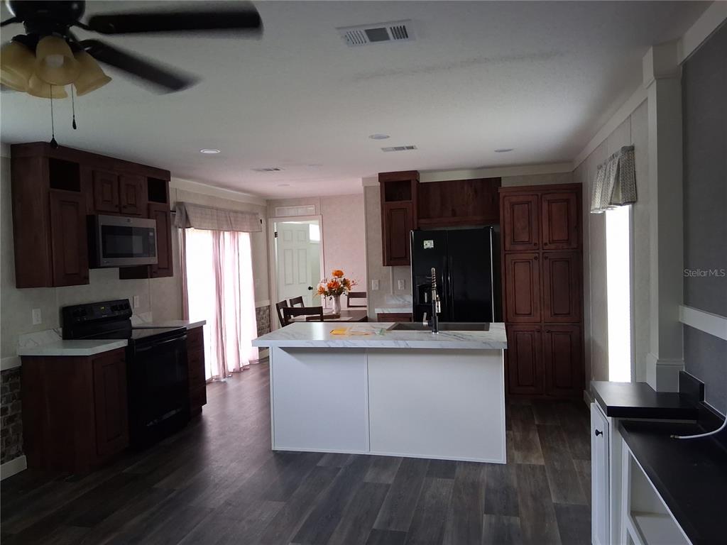 A kitchen features dark wood cabinets, a white island with a sink, and black appliances — 9170 DAN LYNN STREET, BROOKSVILLE, FL