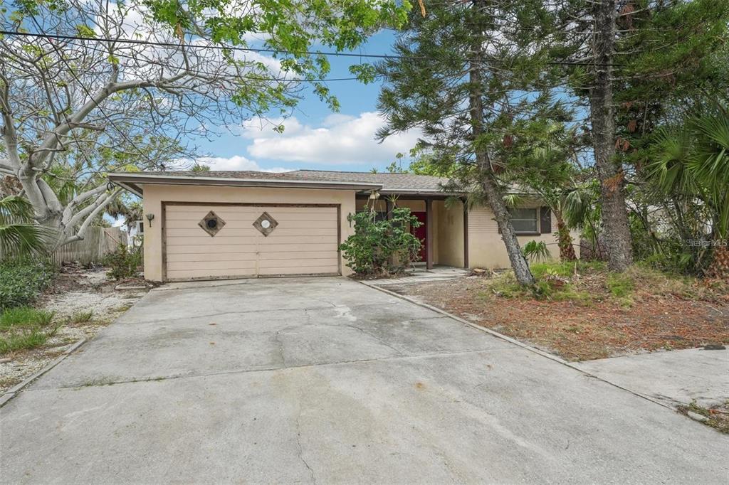 A single-story house with a two-car garage, concrete driveway, and surrounding trees — 9300 GULF BOULEVARD, ST PETE BEACH, FL