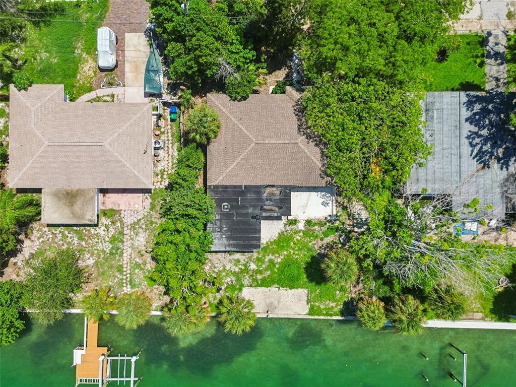 An aerial view shows three waterfront houses with shingled roofs, trees, and a wooden dock — 9300 GULF BOULEVARD, ST PETE BEACH, FL