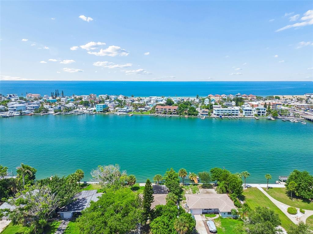 An aerial view shows a waterfront residential area with a turquoise bay and the ocean — 9300 GULF BOULEVARD, ST PETE BEACH, FL