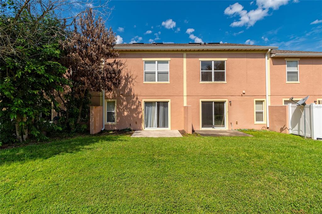 The exterior rear view of a two-story townhouse features a grassy lawn and sliding doors — 3745 COLLINGWOOD LANE, OVIEDO, FL