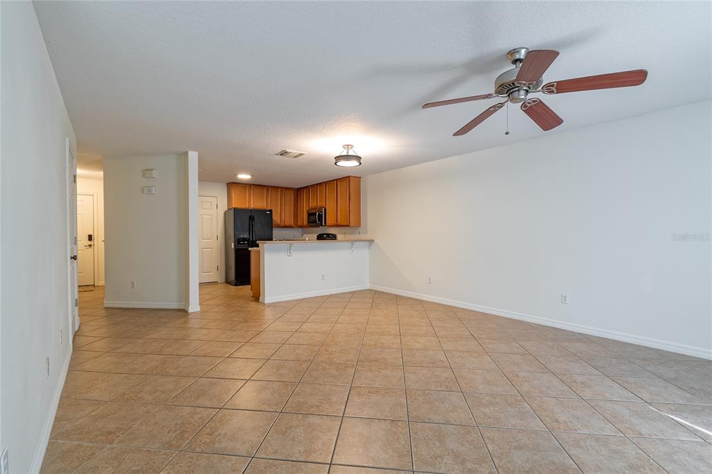 An open-concept kitchen with wood cabinets and a breakfast bar overlooks a tiled living area — 3745 COLLINGWOOD LANE, OVIEDO, FL