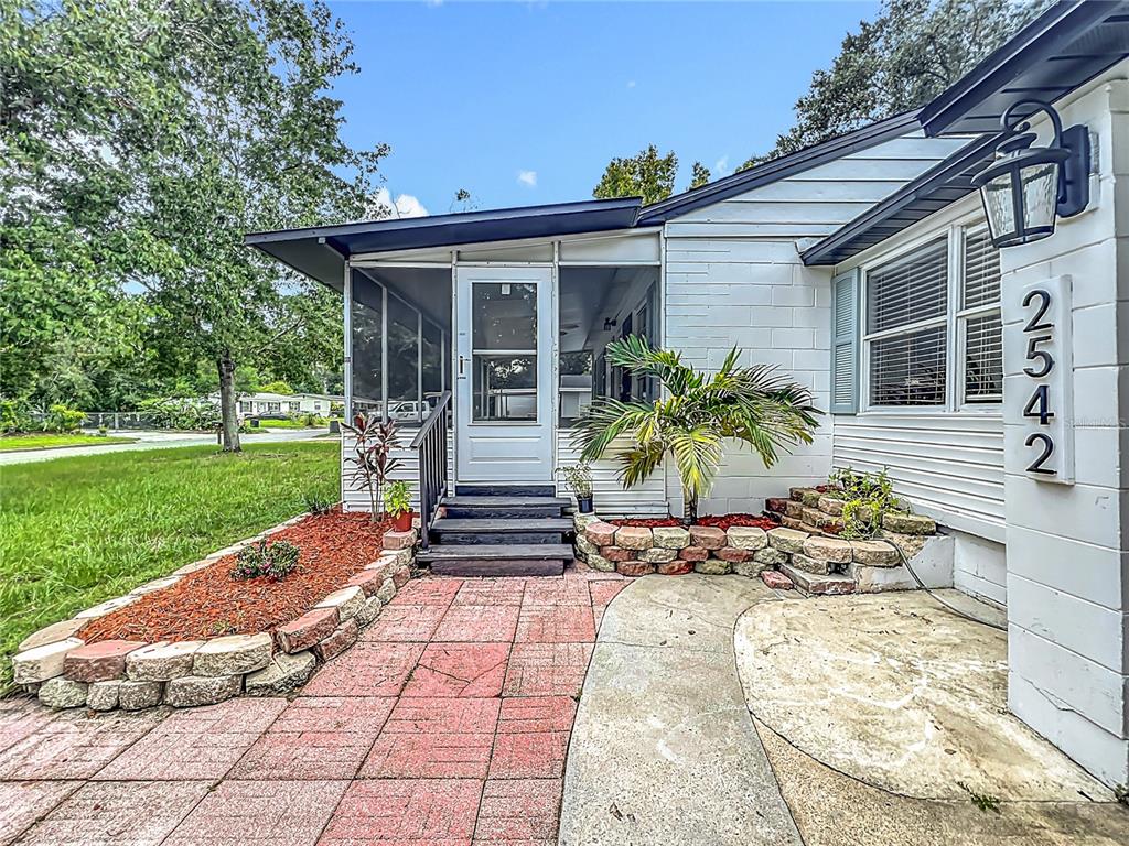 A white house exterior features a screened porch, stone landscaping, and a red paver walkway — 2542 S PALMETTO AVENUE, SANFORD, FL