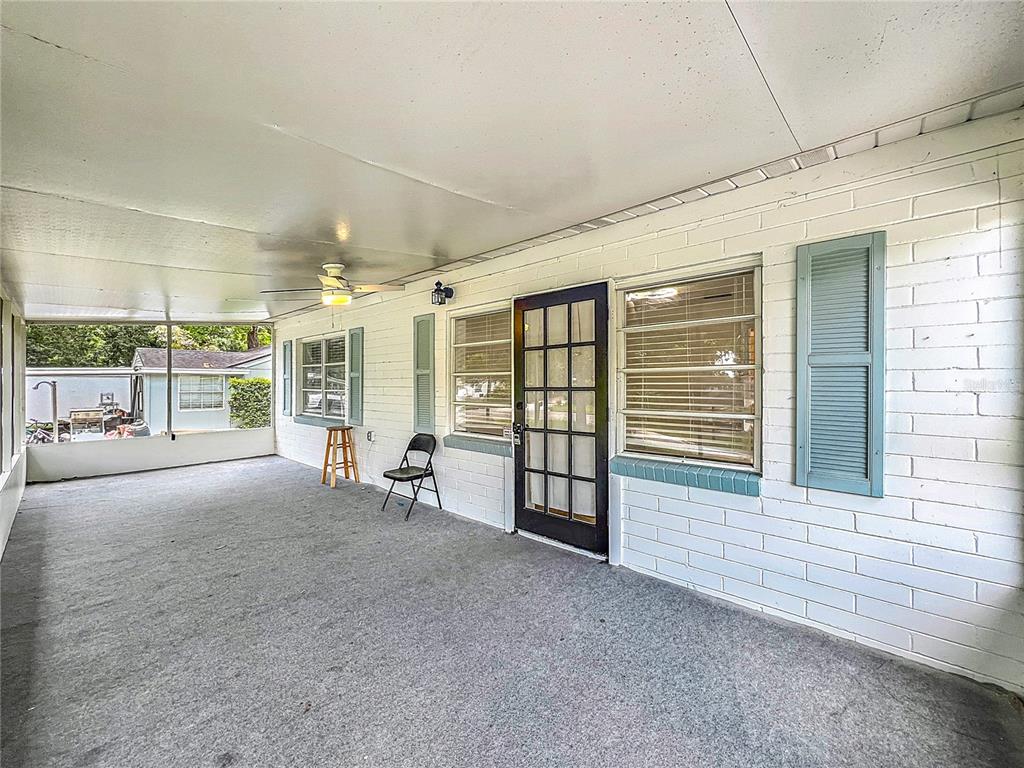 A covered patio features a gray carpeted floor, white brick walls, and a glass-paneled door — 2542 S PALMETTO AVENUE, SANFORD, FL